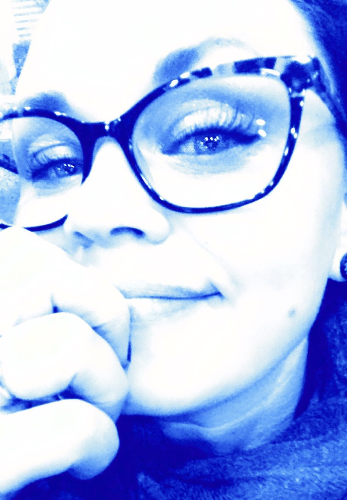 close up blue hued headshot of Genevieve in glasses smiling.