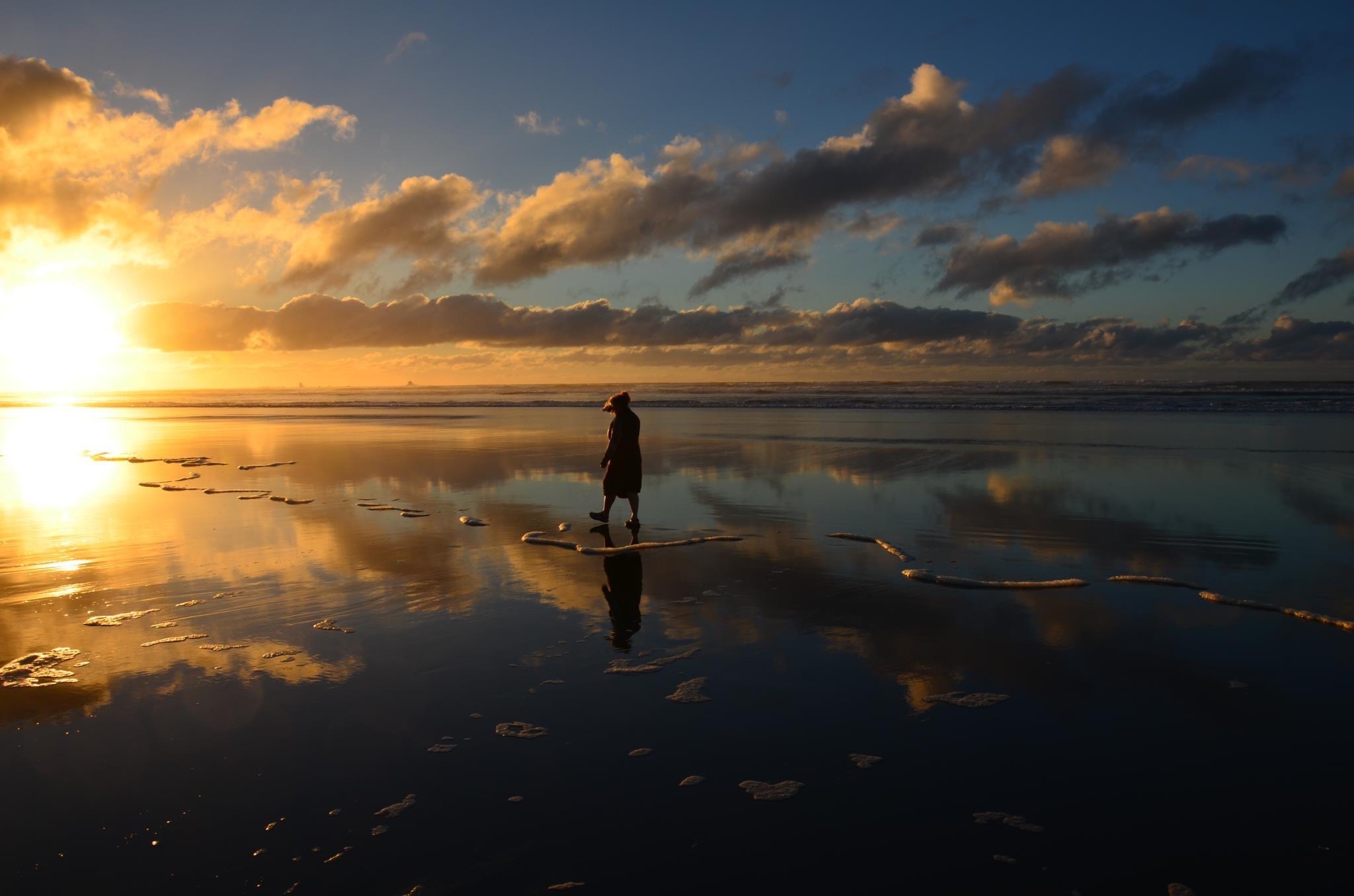 beautiful sunset shot of a beach with a woman in the distance walking barefoot in the sand.